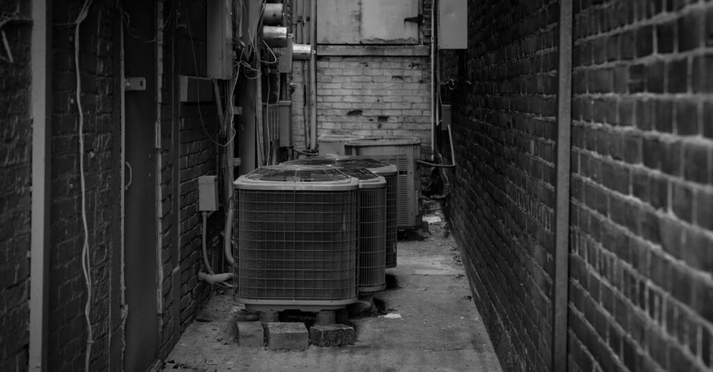 Black and white alley featuring industrial air conditioning units against a brick wall.