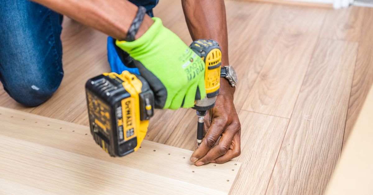 Close-up of handyman drilling wood indoors with green gloves and cordless drill.
