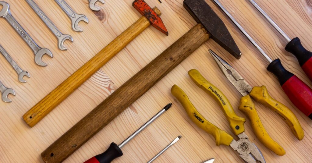 A variety of hand tools including wrenches, screwdrivers, and pliers on a wooden surface.