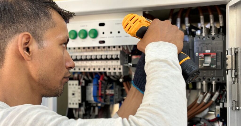 Professional electrician using a drill on an indoor circuit breaker panel.