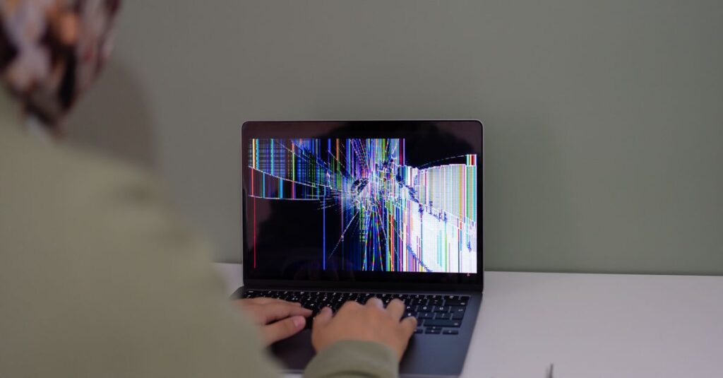 Adult working on a laptop with a cracked screen, indoors setting.