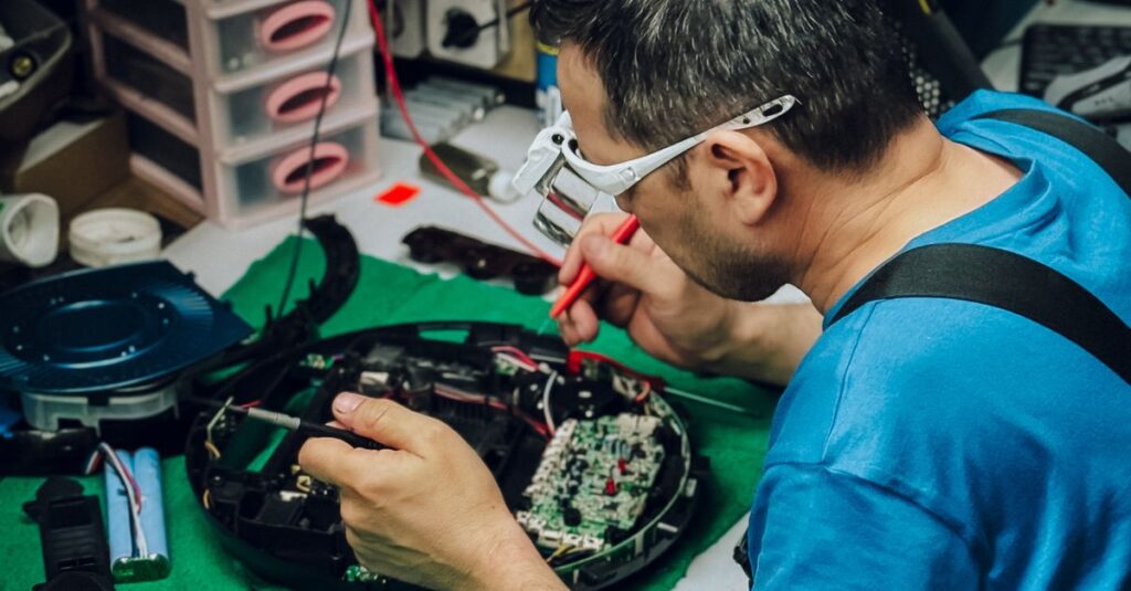 Focused technician repairs electronic device in a cluttered workshop environment.