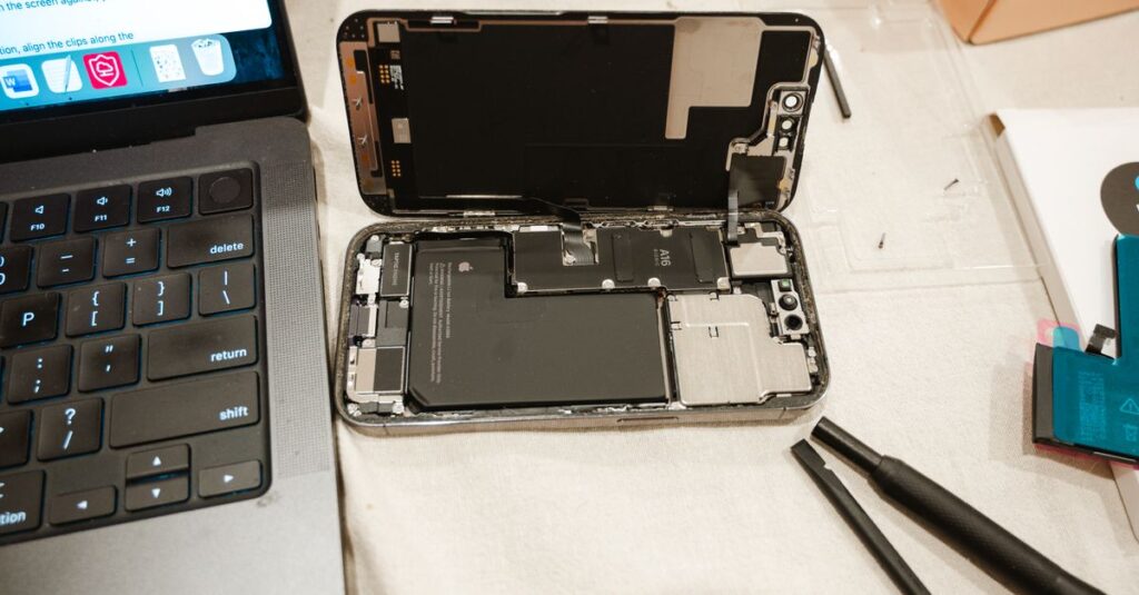 Open iPhone with repair tools and laptop, showcasing DIY battery replacement process.
