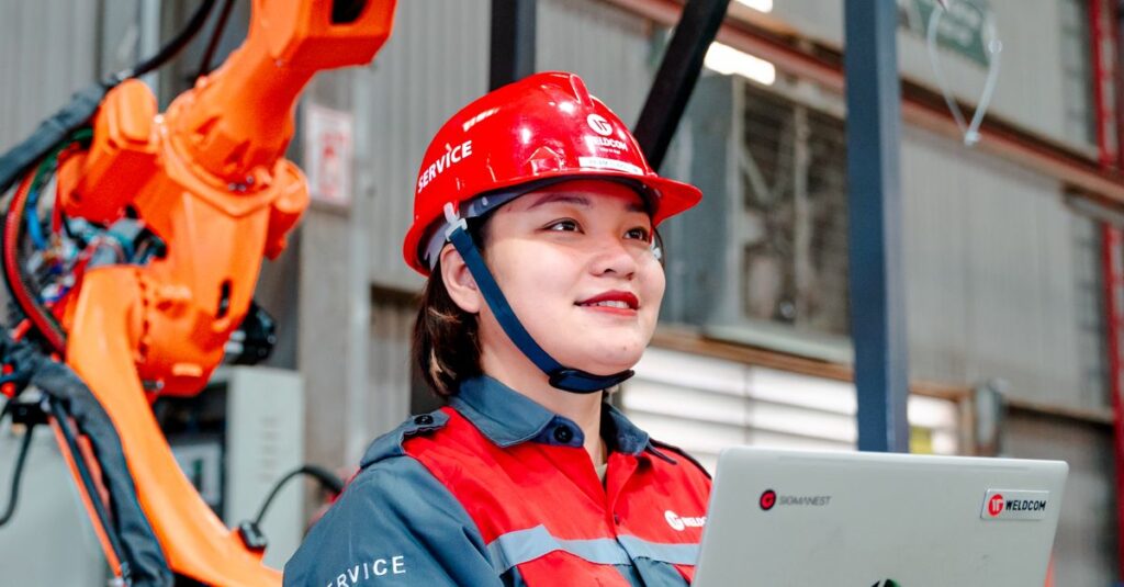 Female engineer with laptop overseeing robotic arm in a manufacturing setting in Vietnam.