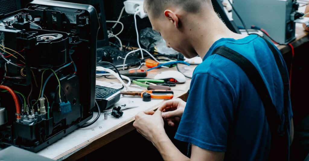Skilled technician seated at a workbench repairing electronic devices in a workshop setting.