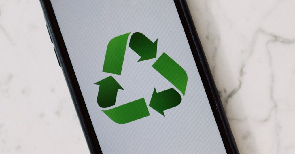 Smartphone placed on marble surface displaying green recycle symbol.