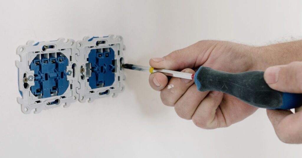 Crop faceless man using screwdriver for installation switches in apartment with light wall in daytime