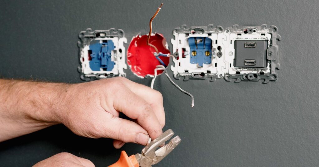 Crop faceless electrician using pliers for installation sockets and switches in new apartment