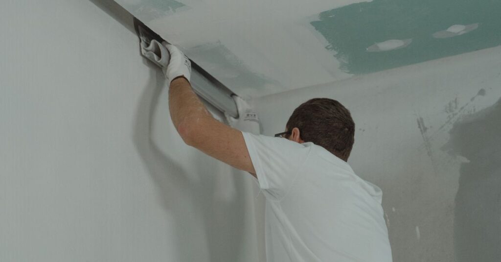 A man works meticulously on drywall installation during a house renovation.
