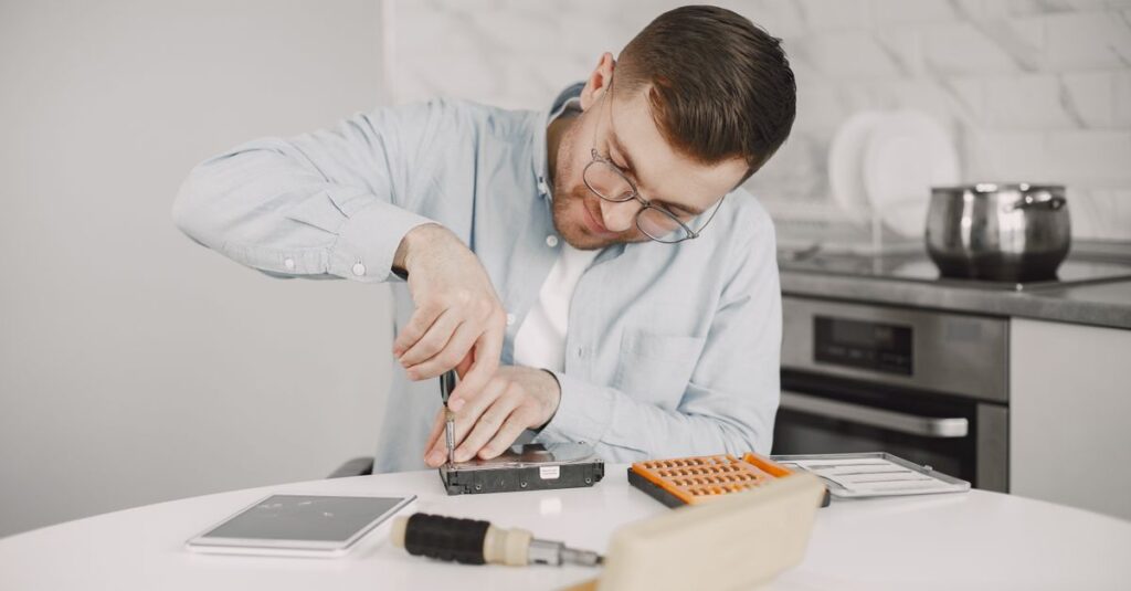 Man wearing glasses using a screwdriver to fix a device on a kitchen table.