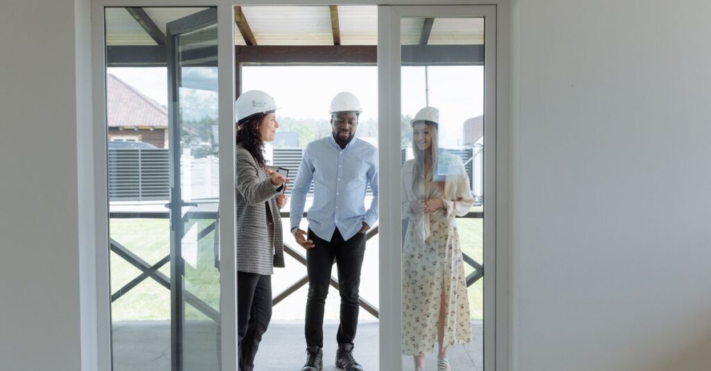 Three real estate professionals in hard hats discussing home features during a house tour.