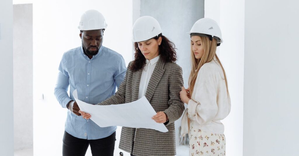Three people in hard hats examining construction plans in a new home's interior.