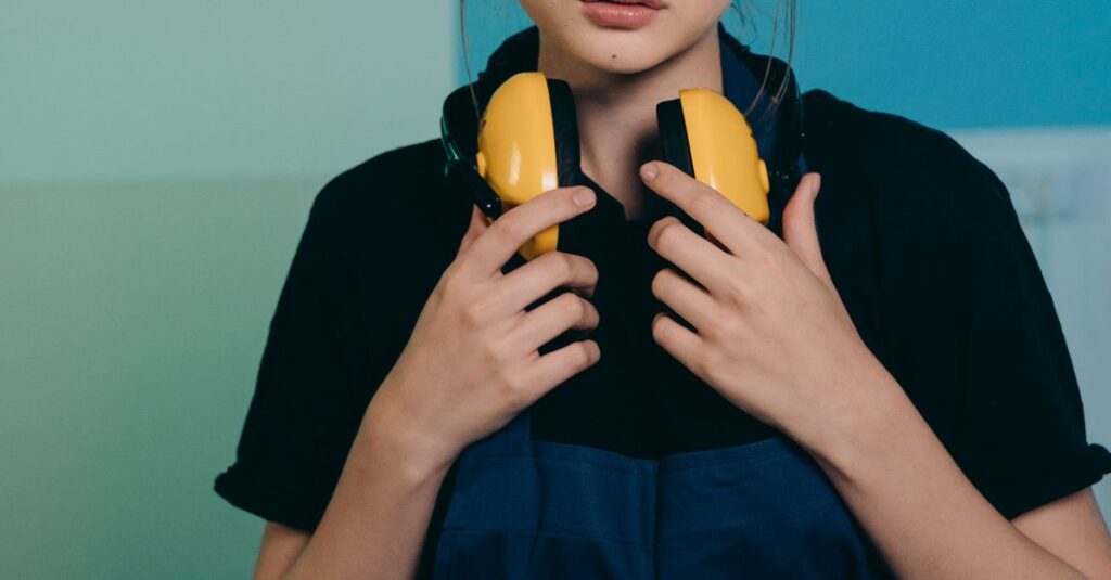 A young caucasian woman wearing safety glasses and ear protection works with electronics indoors.